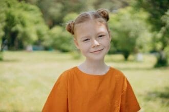 Girl in orange shirt smiling outdoors