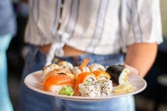 Server presenting a plate of assorted sushi in a restaurant.