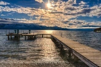 Pier extending into Okanagan Lake at sunset with mountains in the background.