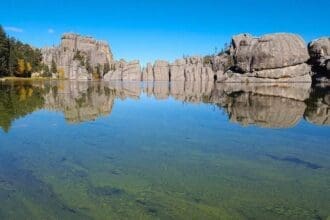 Tranquil forest lake with mirror-like reflection and clear blue sky.